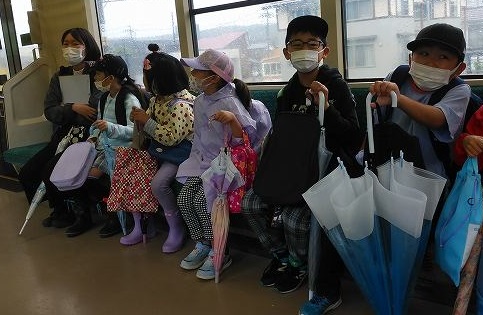 傘を手に、先生と電車の席に座っている児童たちの写真