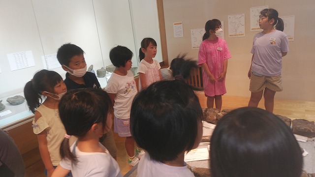 ガラスケースに入れられた展示物の前に集合する児童たちの写真