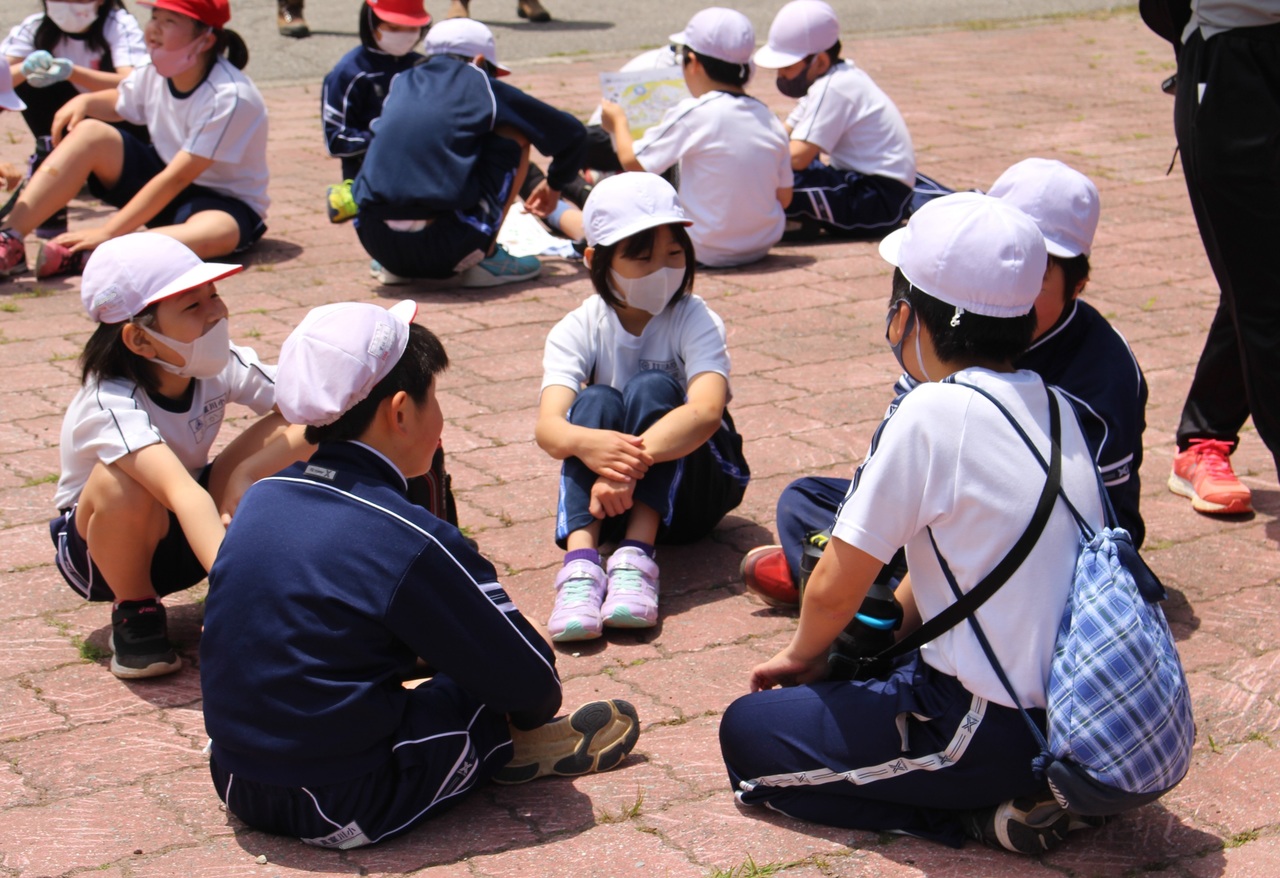 体操帽子を被った子供たちが5人ずつ固まって地面に座り込み、会話している写真
