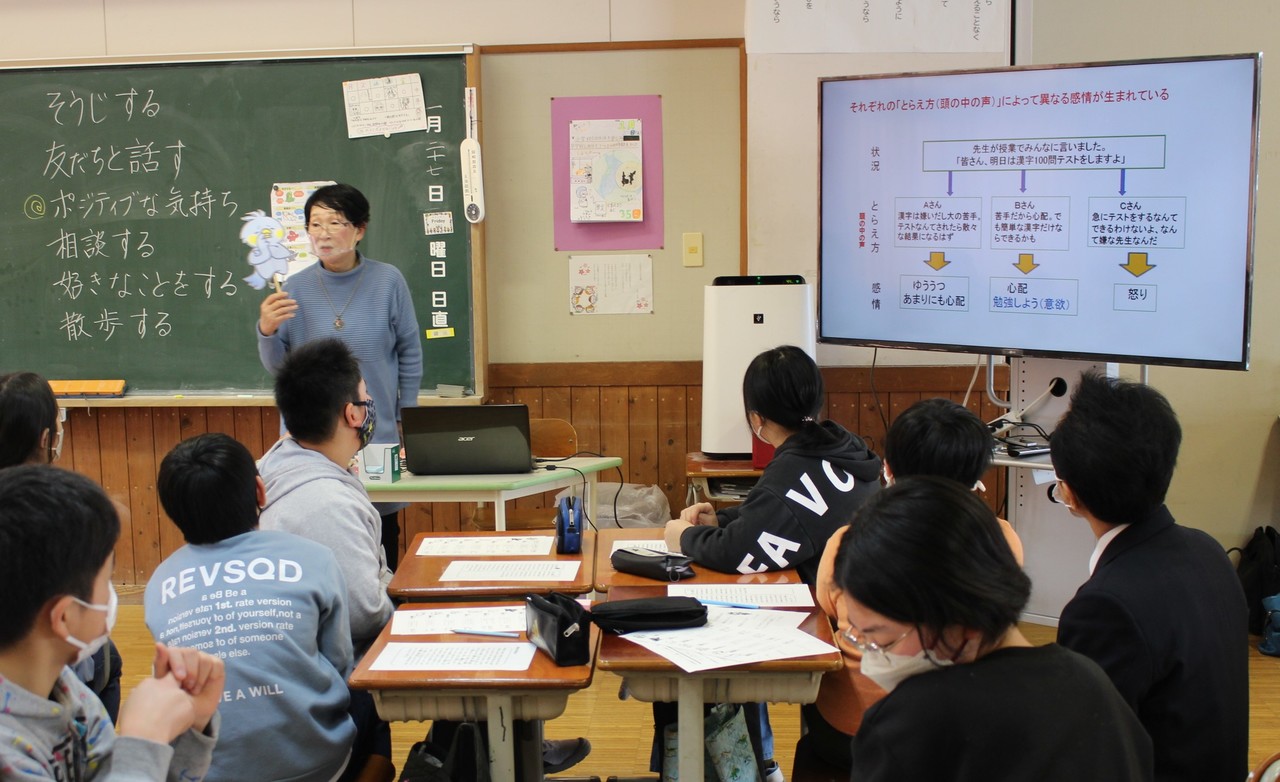 児童たちに対して紙人形の鳥を持って説明している女性の写真