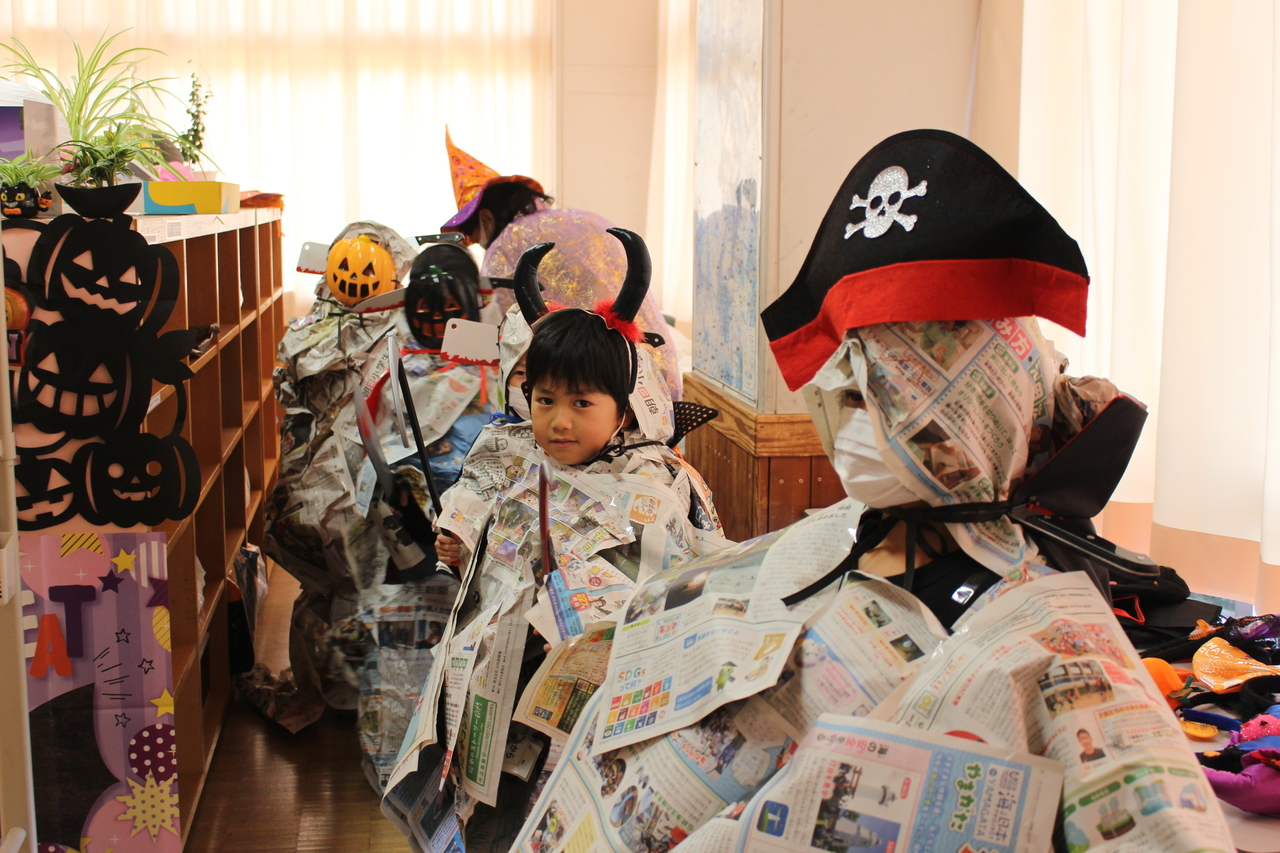 帽子や仮面を被り新聞紙で作られた服を身に着けて並んでいる子供たちの写真