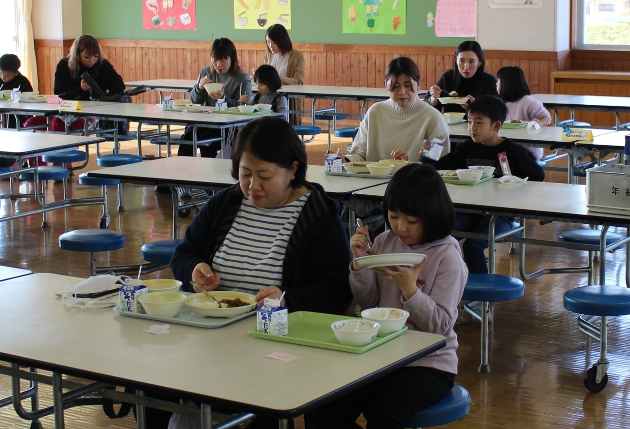 長机で親子が並んで給食を食べている写真