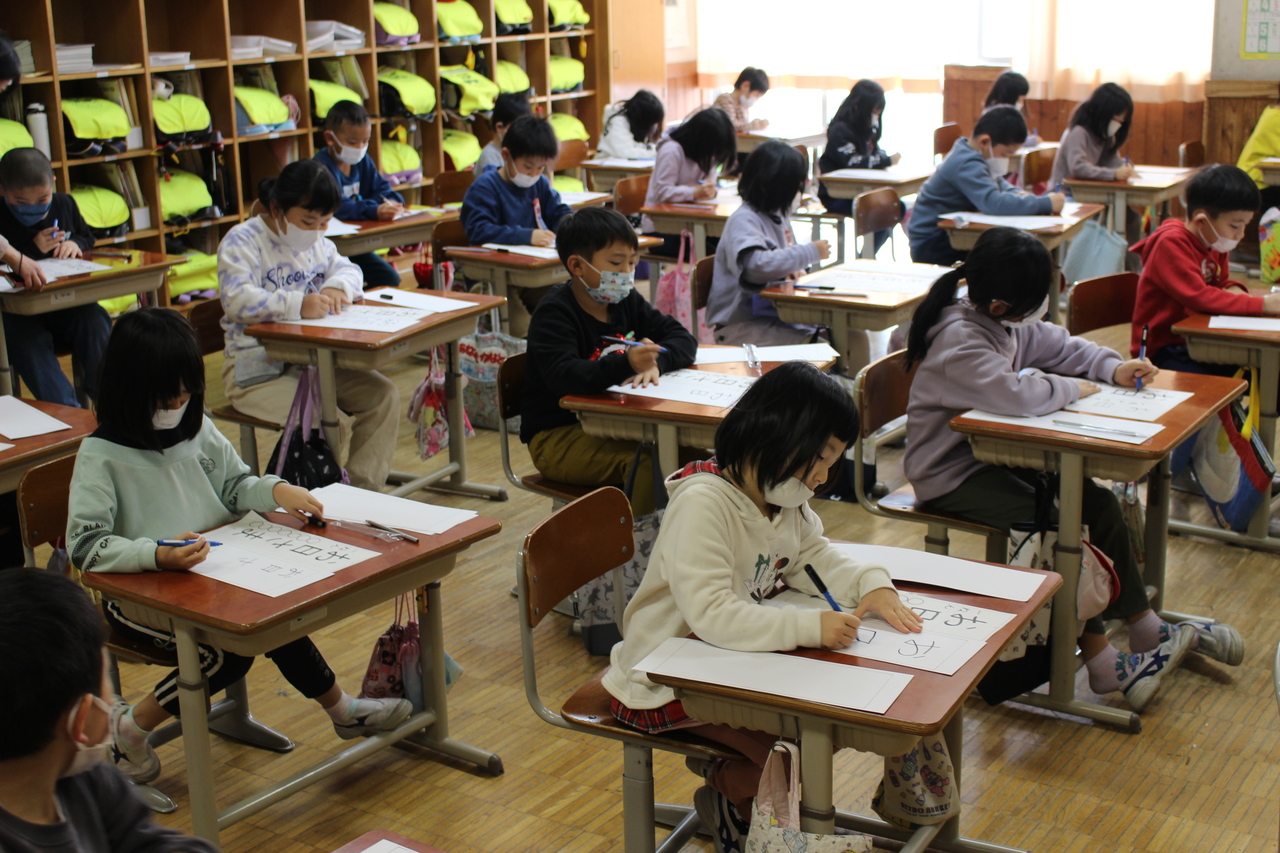 机の上で硬筆で文字を書く児童たちの写真