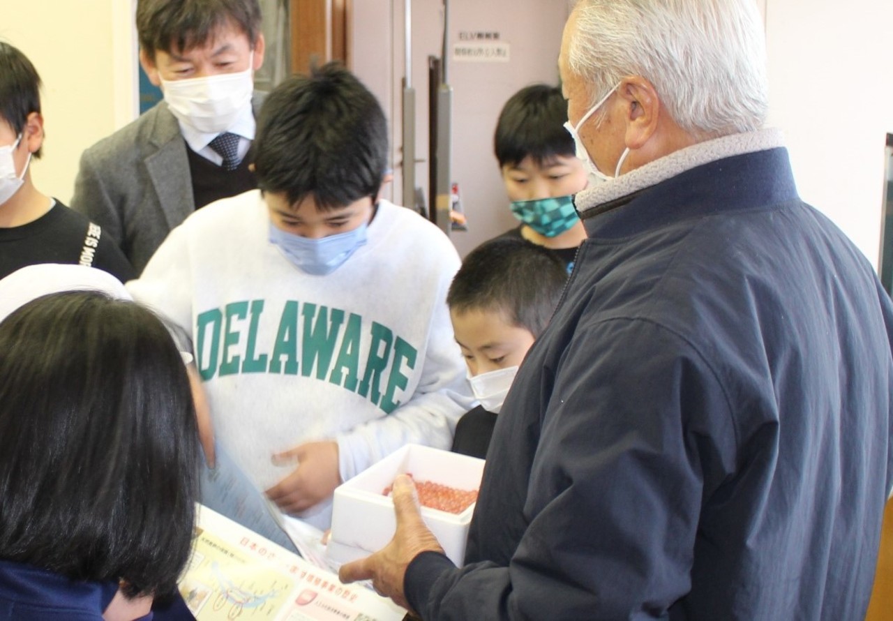 男性が持っている小さな卵が沢山入った発泡スチロールの箱を覗き込む子供たちの写真