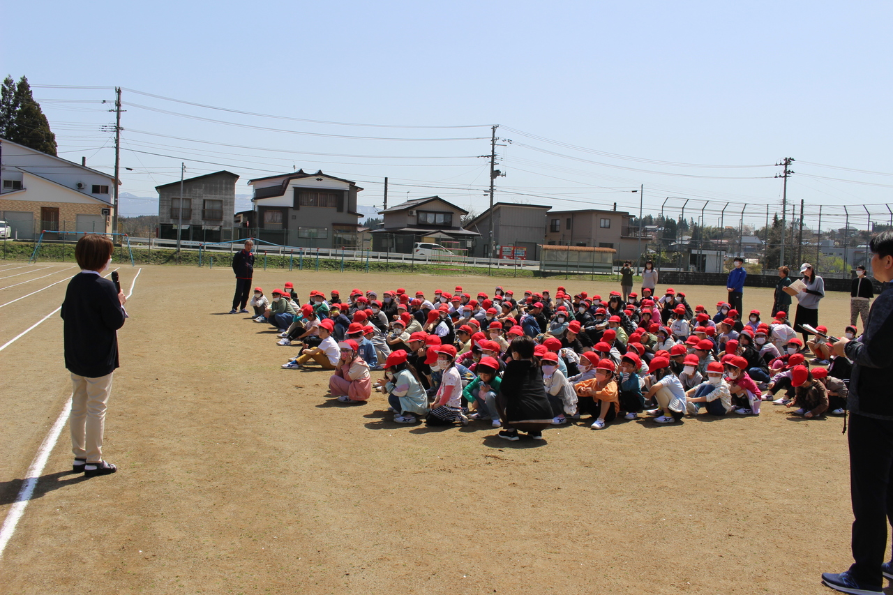 校庭に集まって座り、先生の話を聞いている児童たちの写真