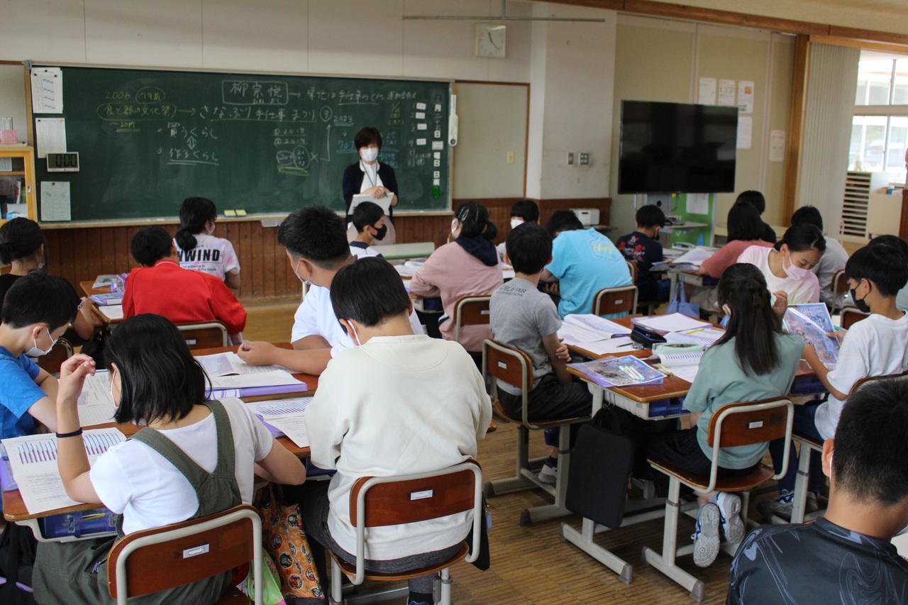 教室内で四人ごとに班を作り先生の話を聞いている生徒たちの写真