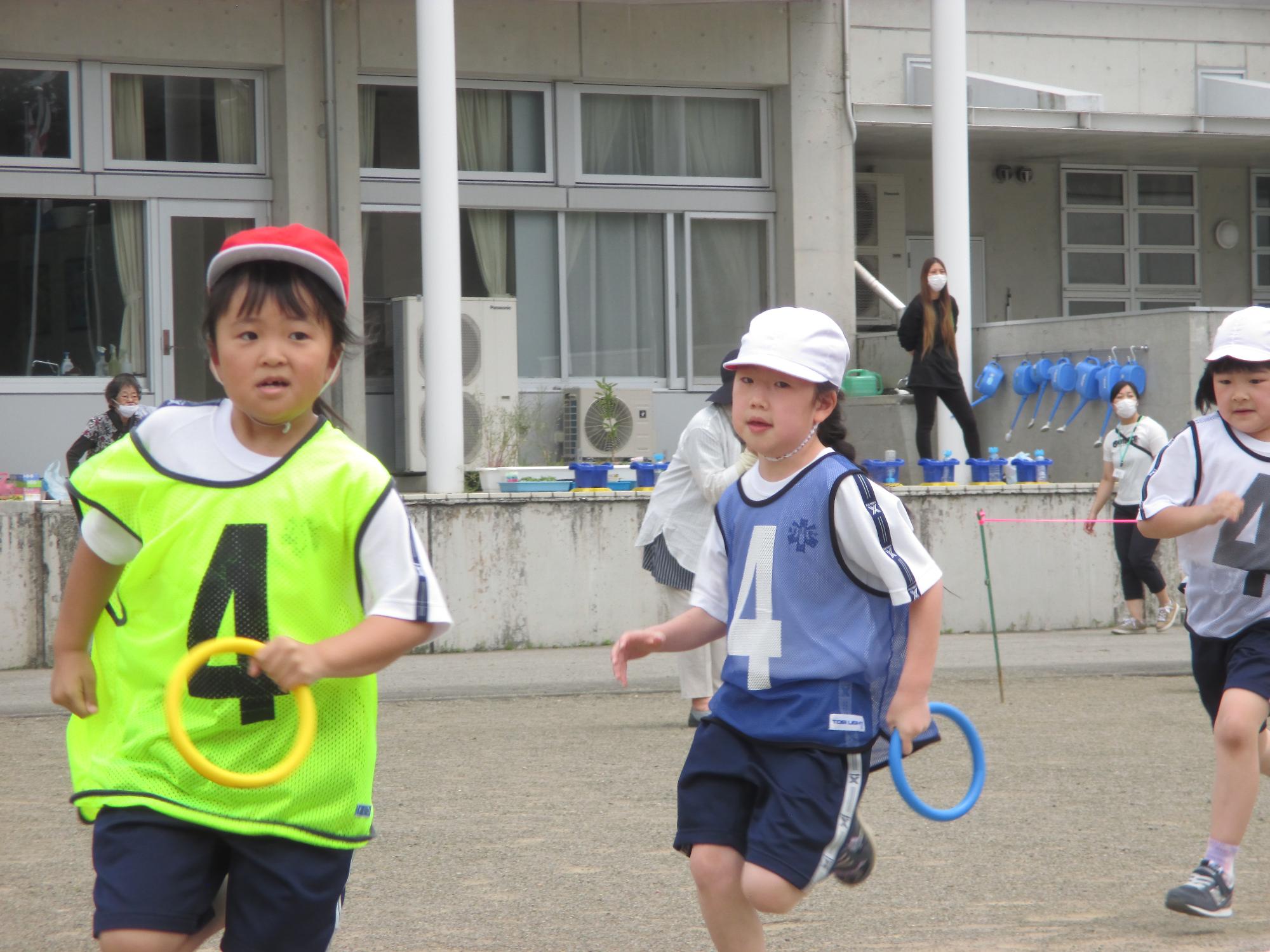 着ているゼッケンと同じ色の輪を持って走る児童たちの写真