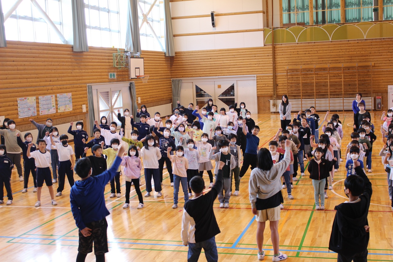 体育館で4人の児童と複数の児童が向かい合って勝鬨を上げている写真