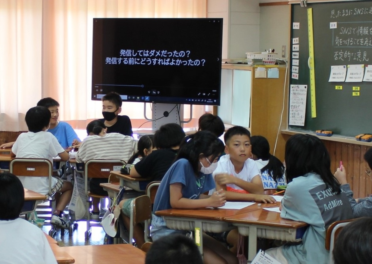 「発信してはダメだったの？発信する前にどうすればよかったの？」と書かれたモニターの前でグループに分かれて話し合う子供たちの写真
