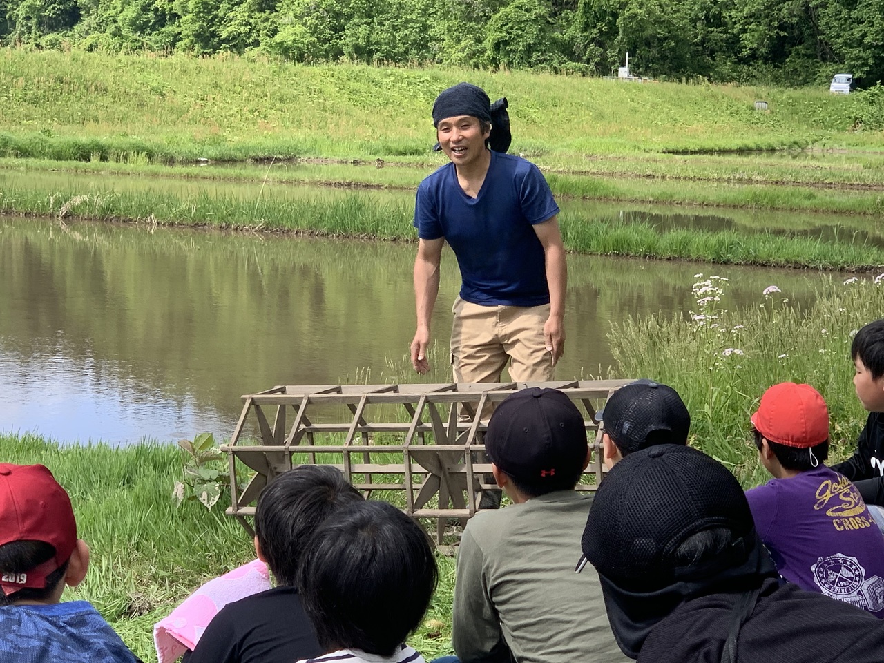 児童たちの前で八角形の筒状をした田植え枠を前に説明している男性の写真
