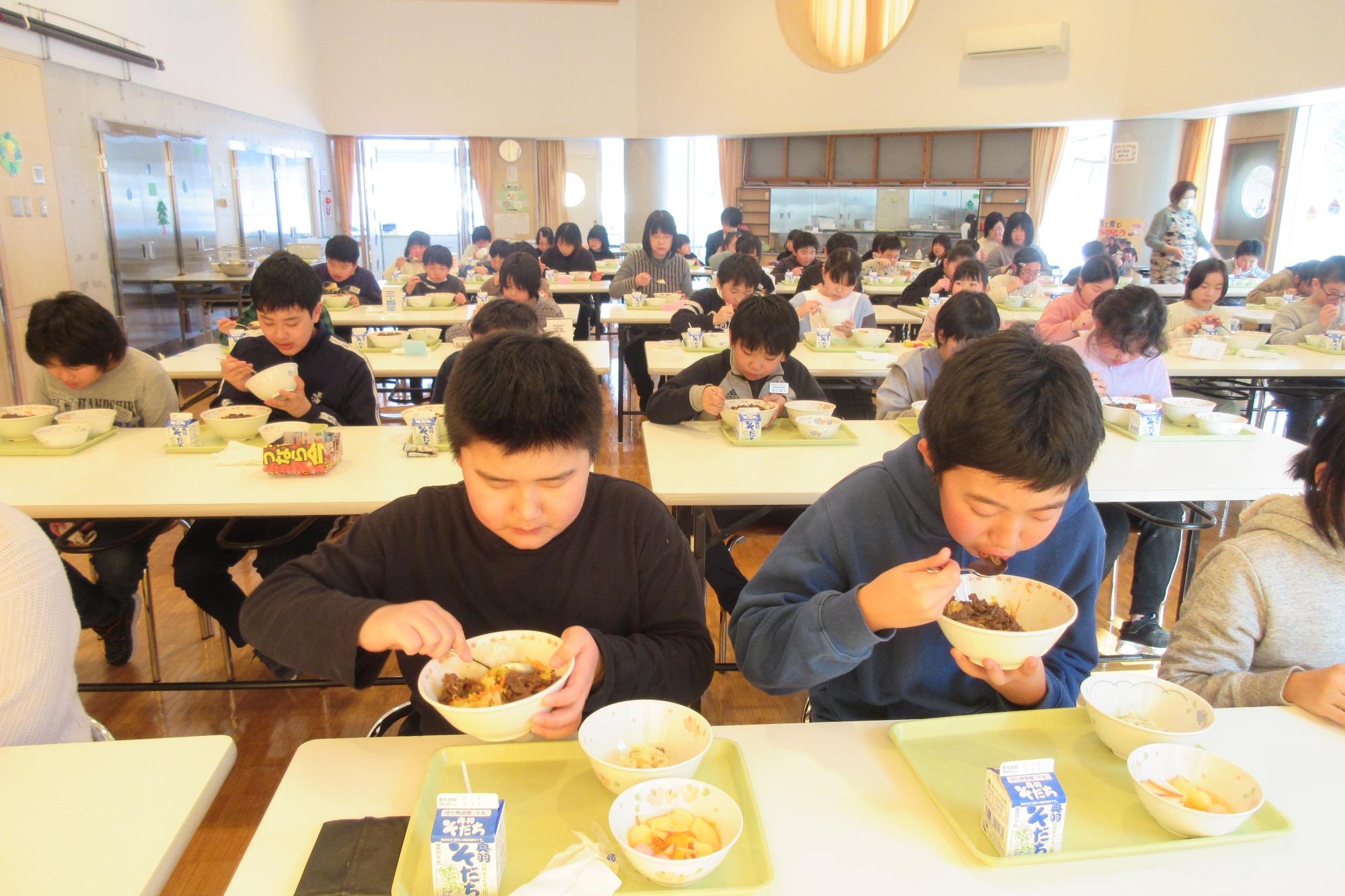 大きな食堂でみんなで給食を食べている様子の写真
