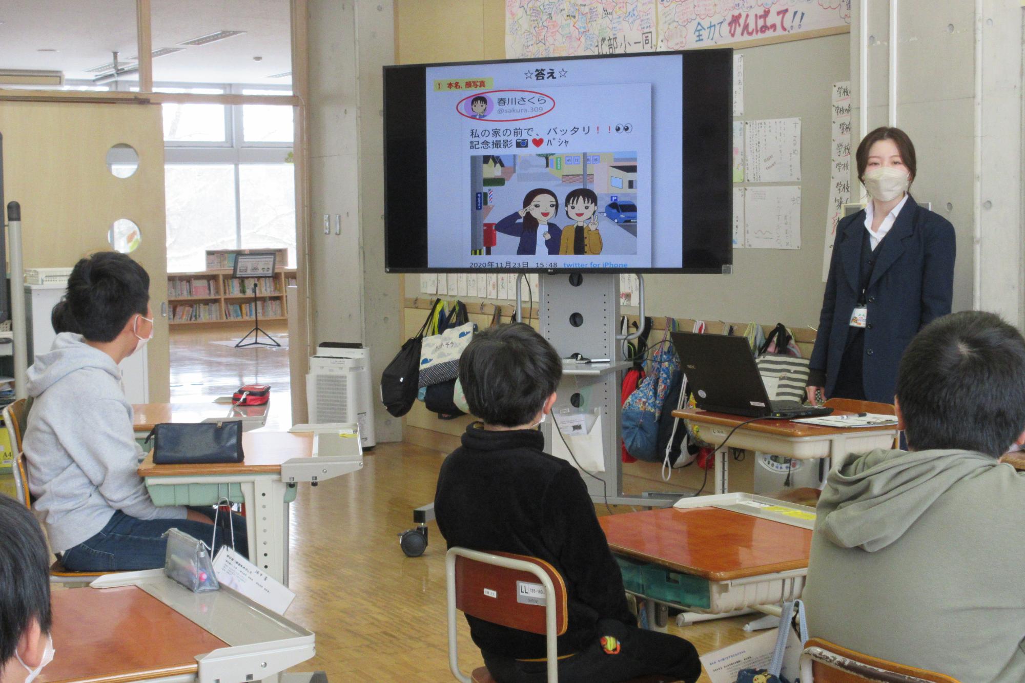 大きなモニターを使って情報モラルについて説明をする講師とそれを座って聞く生徒たちの写真