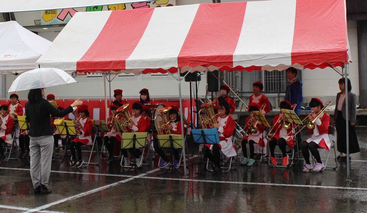 雨の中テントの下で演奏をする児童たちの写真