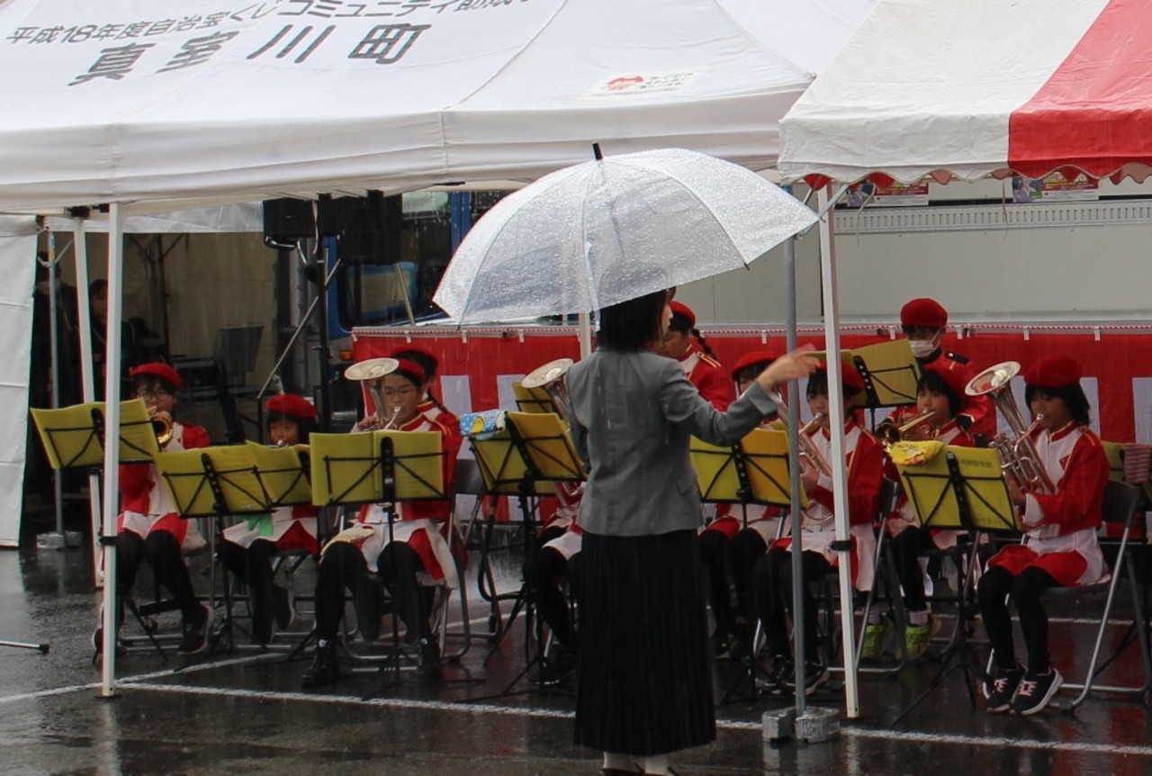 真室川町と書かれたテントの下で演奏をする児童たちの写真
