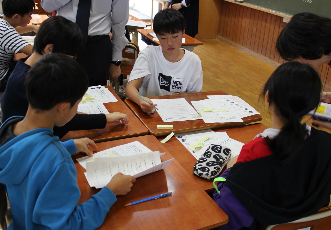 四つ集めた机を囲むように座りプリントに書き込みをしている子供たちの写真