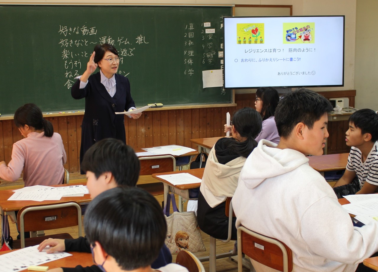 黒板の前に立って話をしているスーツ姿の女性の写真