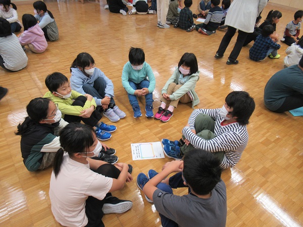 子供たちが円状に集まり床に体育座りをしている写真