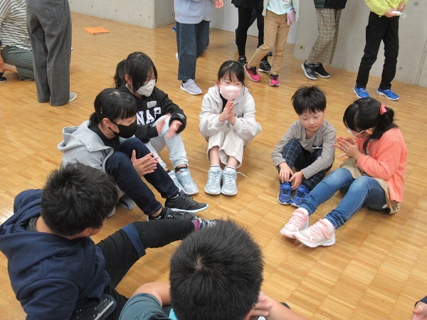 子供たちが円状に集まり床に体育座りをして手を叩いている写真