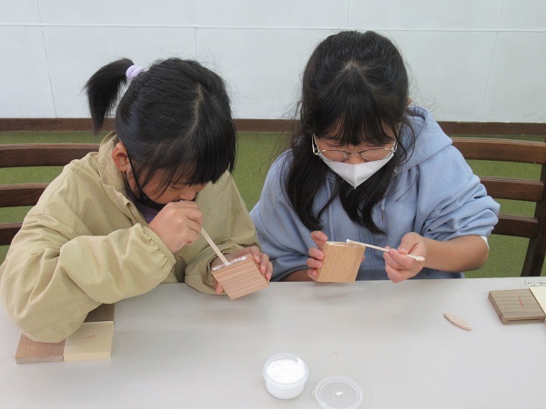 小さな女の子2人が小さな木材にボンドを塗っている写真