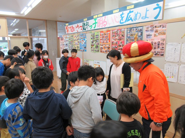 王冠帽を被ってサングラスをかけている男性の前に子供たちが集まっている写真