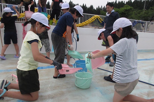子供たちがチリトリで掬った水をバケツに入れている写真