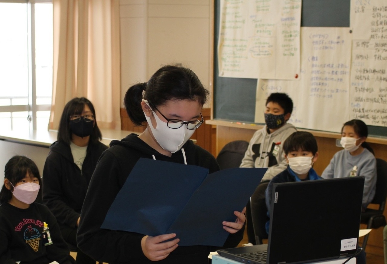 ノートパソコンの前で紙を見ながら立つ女の子の写真