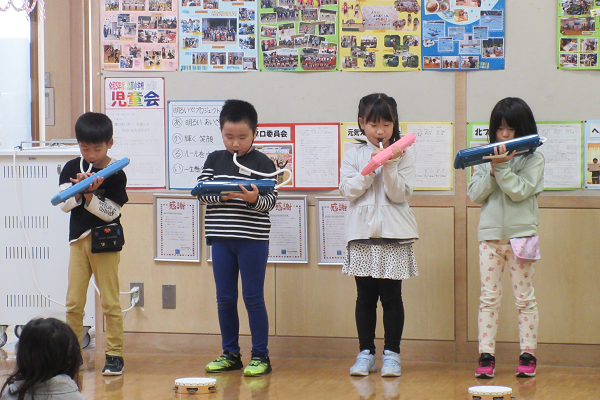 4人の男女の子供たちが立ちながらピアニカを演奏している写真