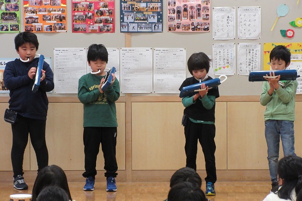 4人の男の子たちが立ちながらピアニカを演奏している写真