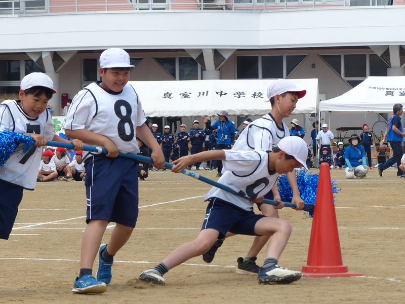 長い棒を四人がかりで抱えながらグラウンドを走っている男子児童四人の写真