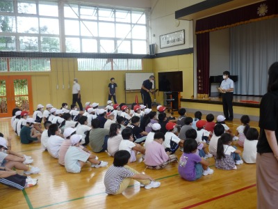 体育館の床に座り、校長先生からの震災時避難についての話を聴く児童たちの写真