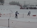 前方の選手を追いかけるように平らな雪原をスキーで進む児童の写真