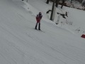 ストックをわきに抱えるようにクラウチング姿勢で坂を滑り降りる別の児童の遠方写真