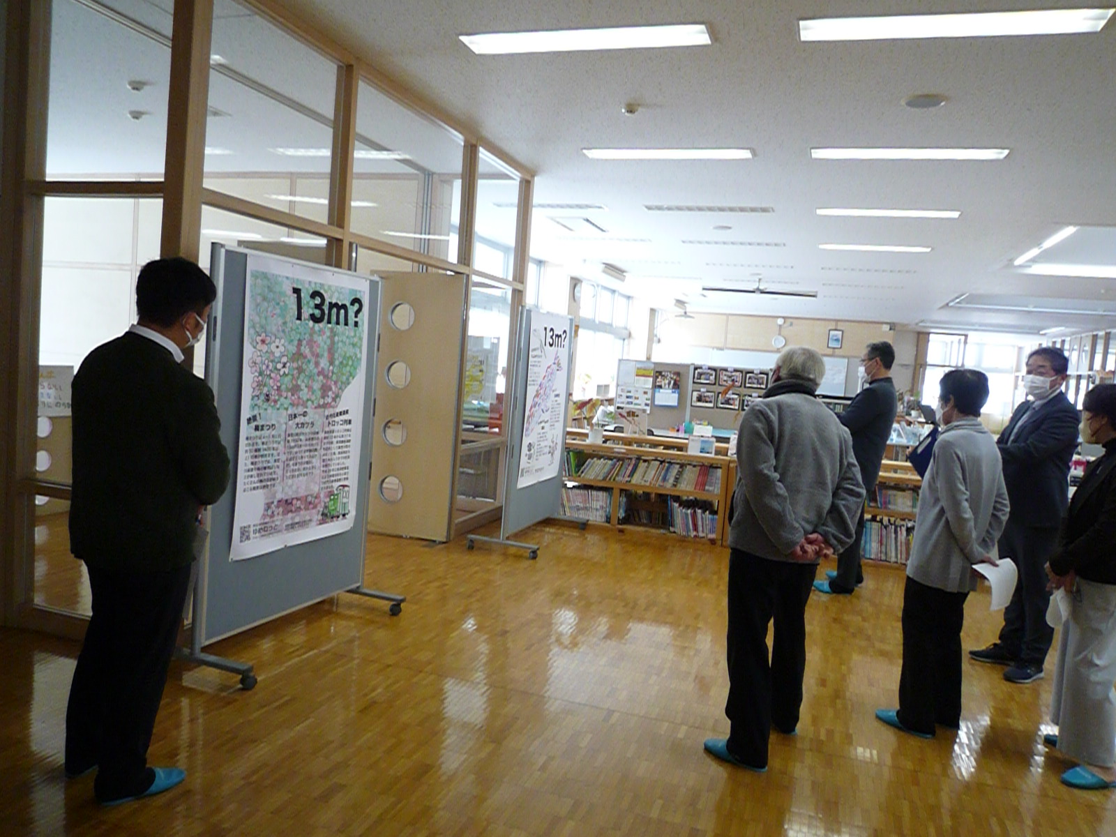 図書室に掲示された5・6年生が作成した真室川町PRポスターを見る運営協議メンバーの写真