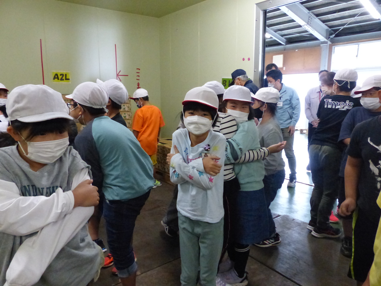 赤白帽を被ってマスクをした大勢の子供たちが腕を抱えて寒がっている写真