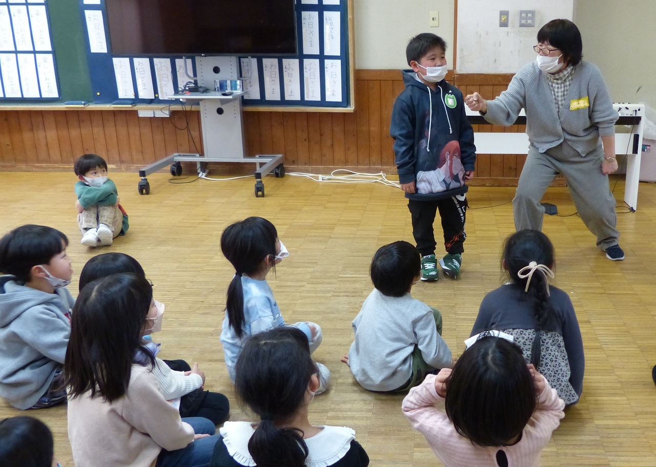 男の子にインタビューする女性とそれを座って見ている子供たちの写真