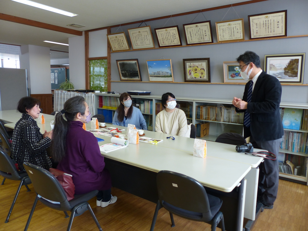 席についた4人の女性と立っているスーツ姿の男性が向かい合って話をしている写真