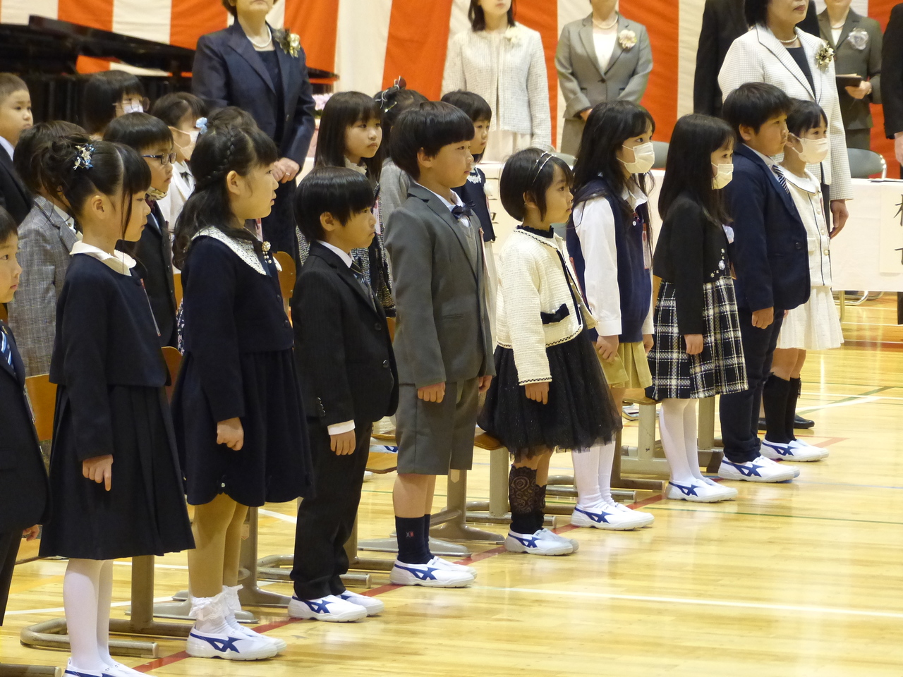 スーツやブラウス姿で一列になって並んでいる児童たちの写真