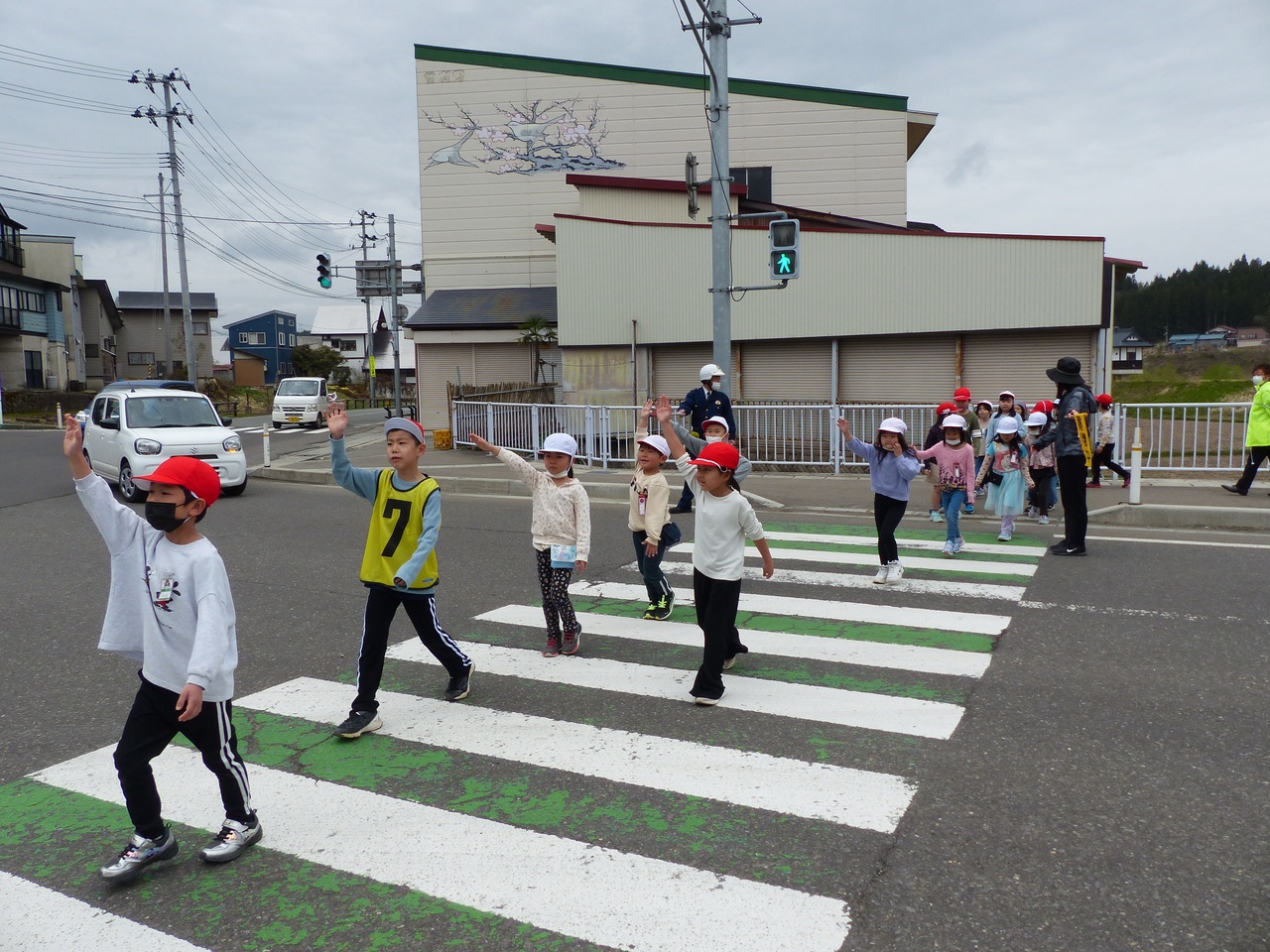 体育帽子を被った児童たちが横断歩道を片手を上げながら渡っている写真