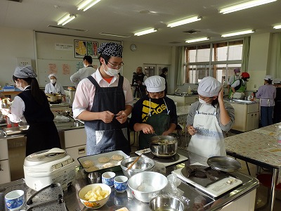 先生の指導を受けながら、鍋で煮物をする男子児童と女子児童の写真