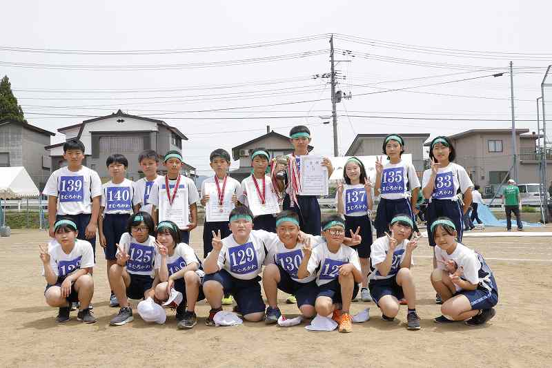 メダルを首にかけたり、賞状を手に持ったりして、グラウンド上でポーズをとる、真室川あさひ小学校児童たちの写真
