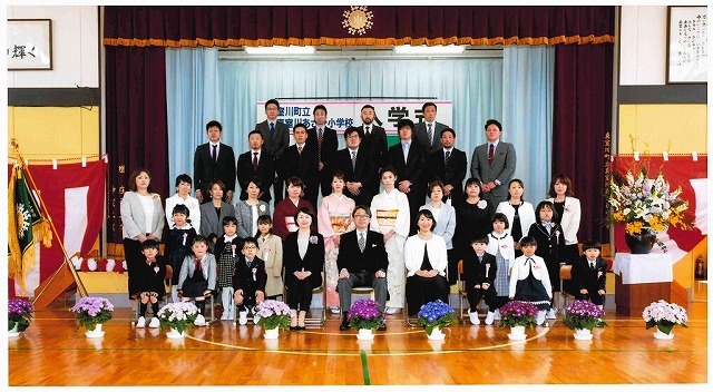 体育館の舞台前で新入生たちと先生たちが整列して撮った記念写真
