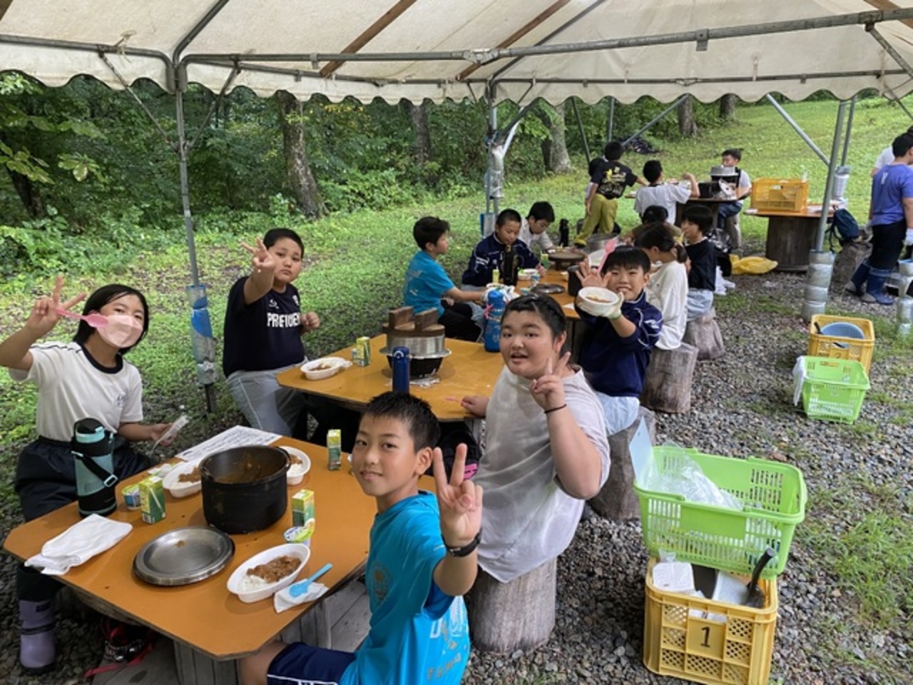 カレーを食べながらカメラに向かってピースサインをする子供たちの写真
