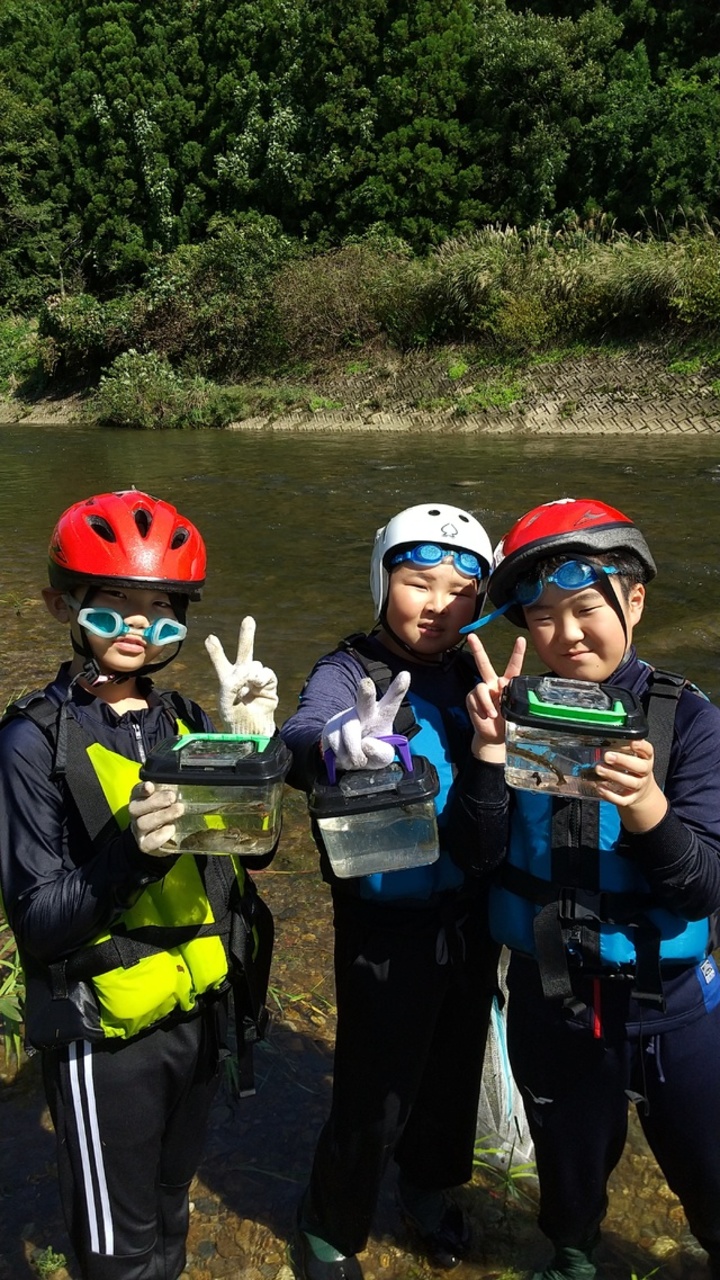 小魚が入った水槽を見せながら笑顔でピースサインをする子供たちの写真