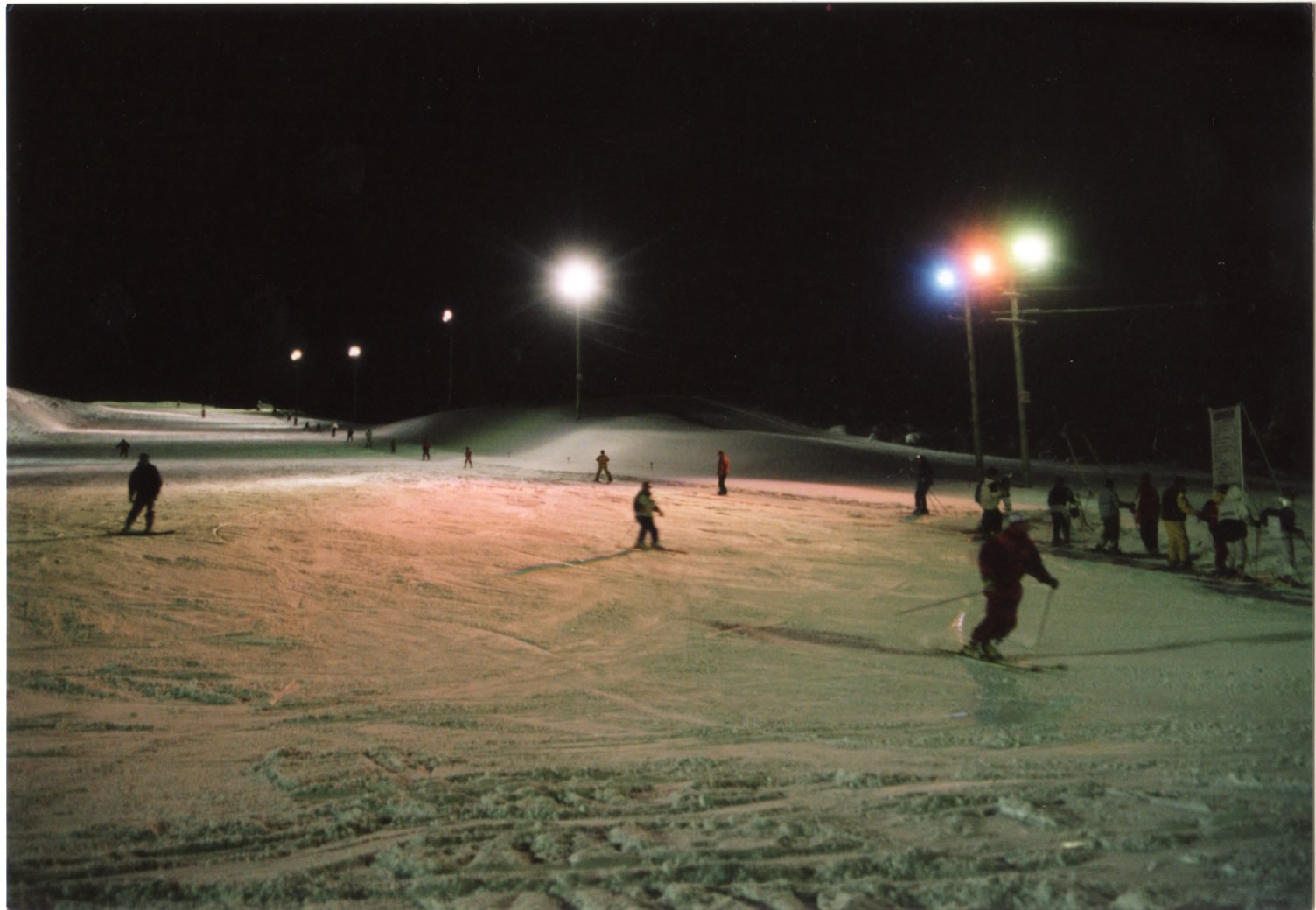 照明に照らされたゲレンデでナイタースキーを楽しんでいる人たちがいる秋山スキー場の写真